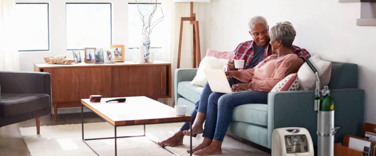 Couple sits in living room next to portable oxygen concentrator